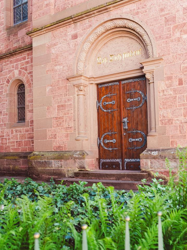 Der Haupteingang der evangelischen Dorfkirche Bammental aus rotem Sandstein mit der goldenen Inschrift »Laß Dich finden!« über dem Portal.