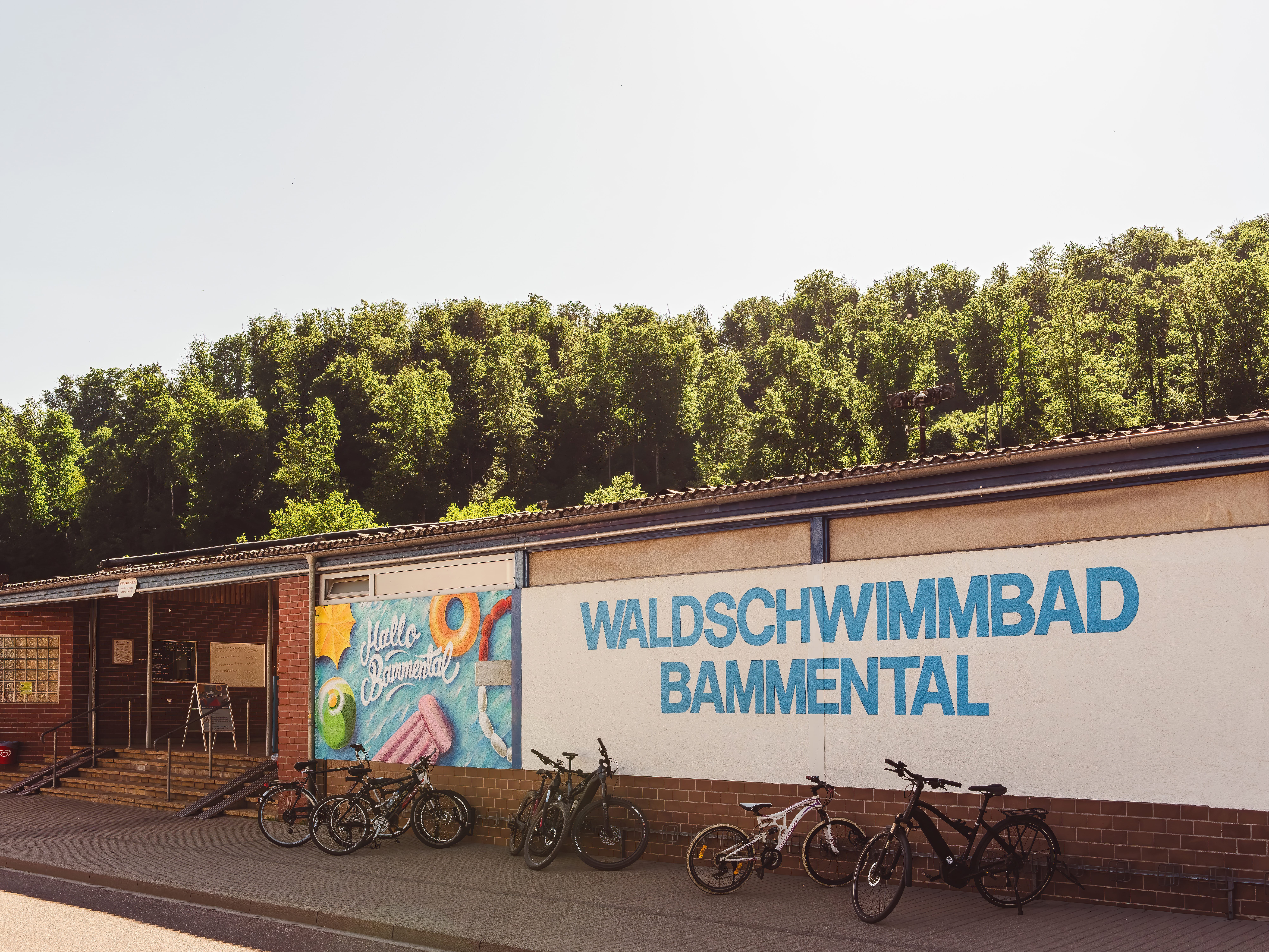 Der farbenfrohe Eingang zum Waldschwimmbad Bammental mit dem „Hallo Bammental“-Mural und Fahrradständern – idealer Sommerspot am Waldrand.