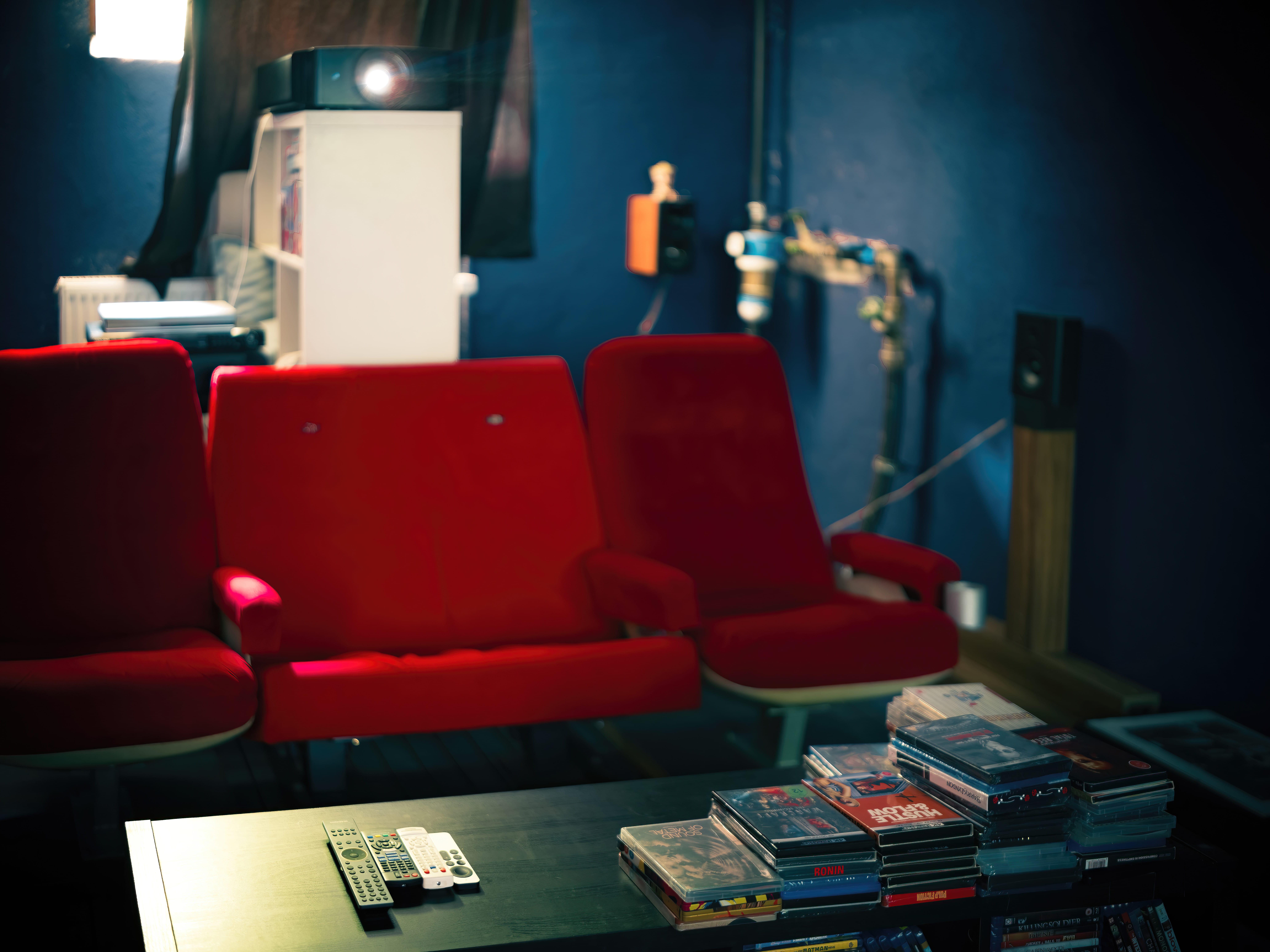 Heimkino mit roten Kinosesseln, JVC Projektor und großer Filmsammlung in Regalwand.