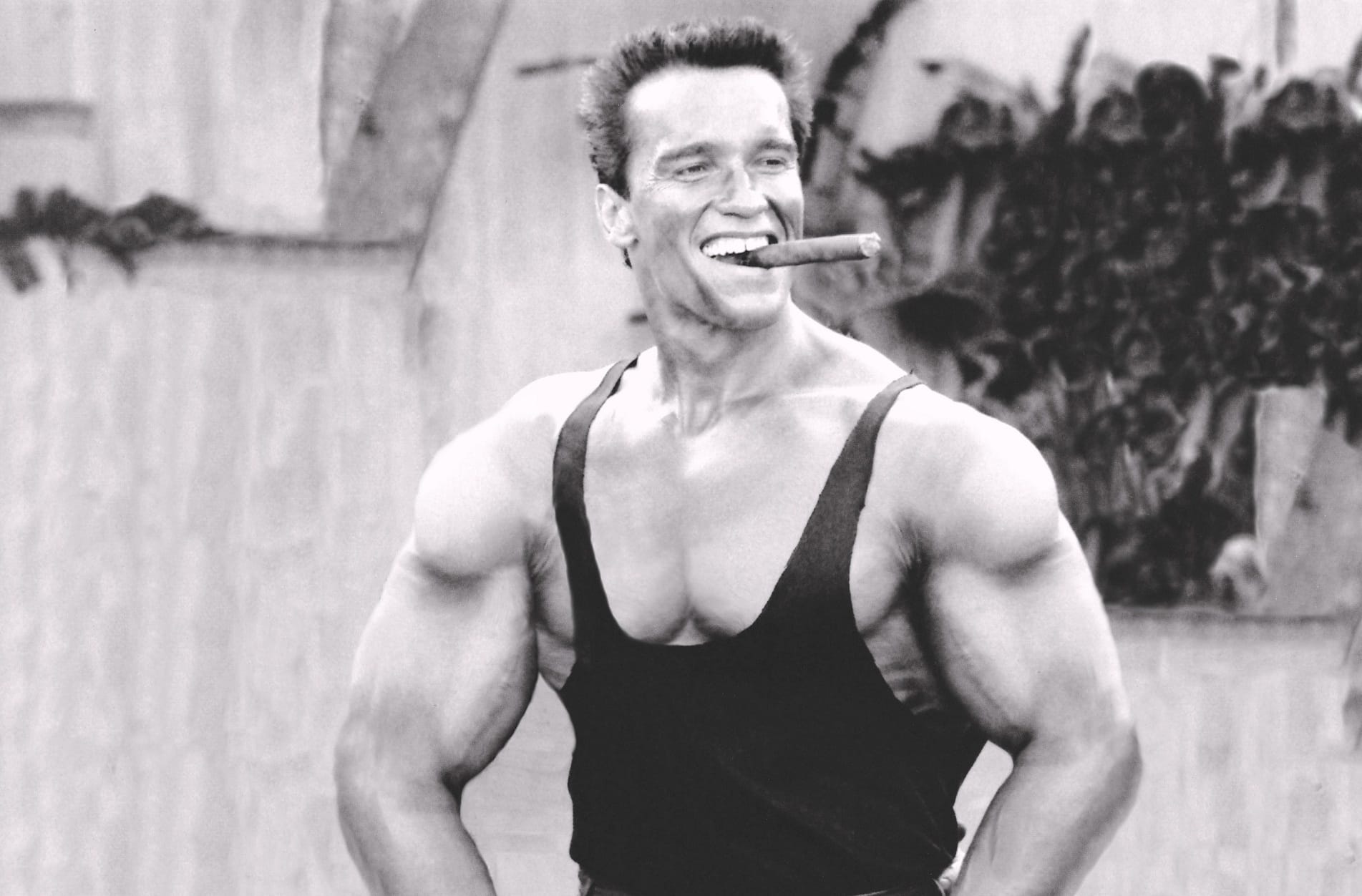 Arnold Schwarzenegger flexing muscles and smoking a cigar during bodybuilding era