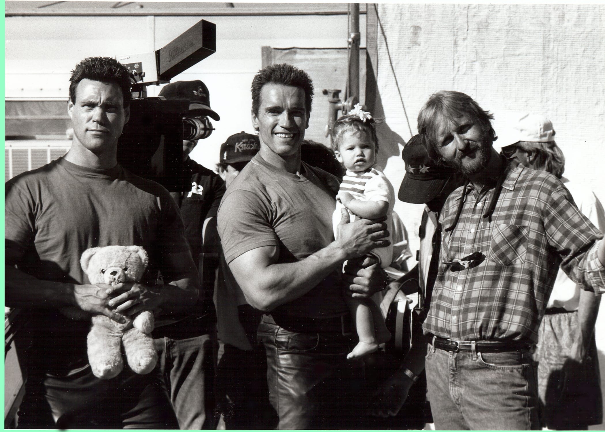 Arnold Schwarzenegger holding baby with James Cameron on Terminator 2 set